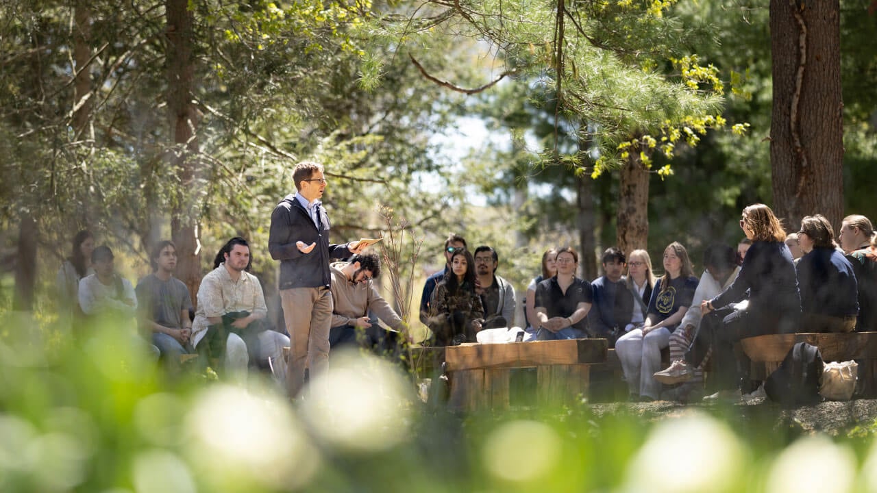 A professor talks to his students outside in a forest