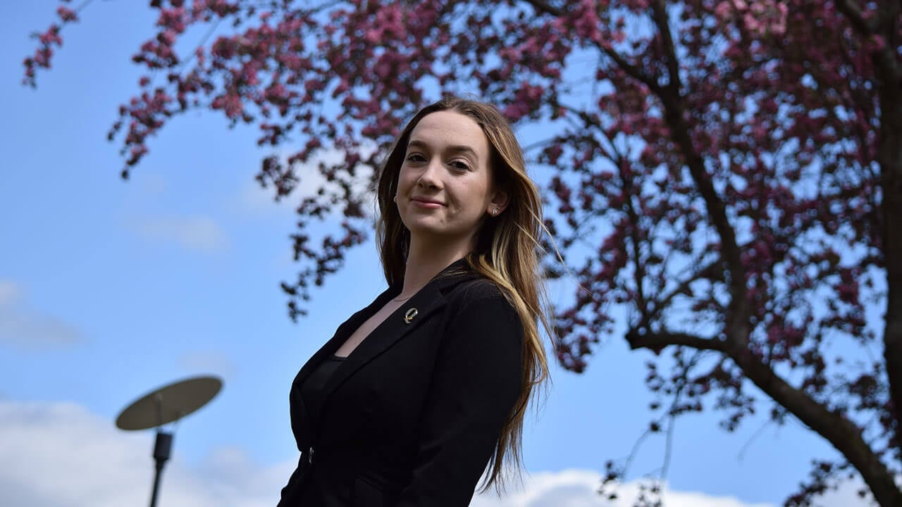kaitlyn sternhardt poses for a picture under a pink blossomed tree