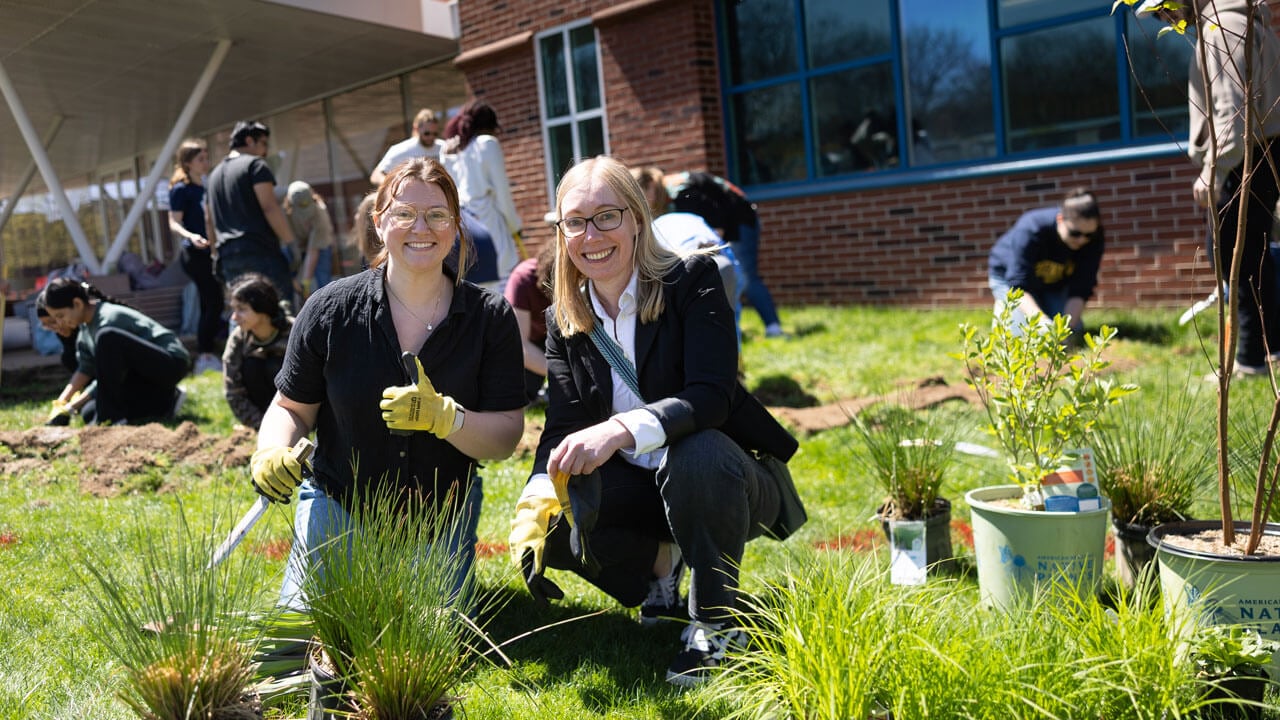 Professor and her student smile as they garden outside