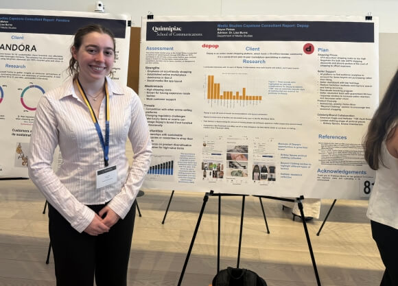 Brynn Pinkes standing in front of a poster board during a symposium.