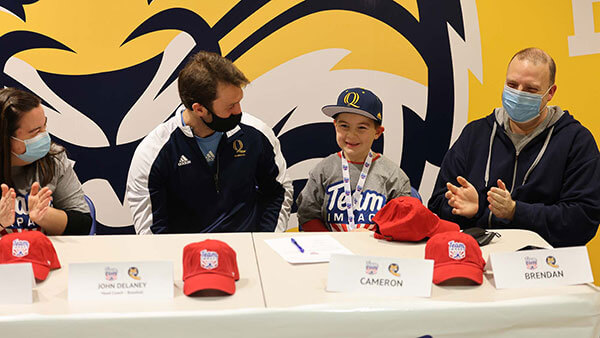 6-year-old Cam sits at a table with his father, mother and QU baseball coach after signing his letter with the baseball team.