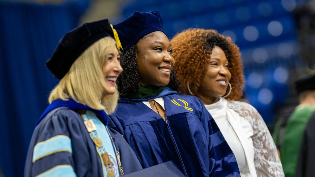 President Marie Hardin smiles alongside a 2026 School of Medicine graduate and her loved one on stage