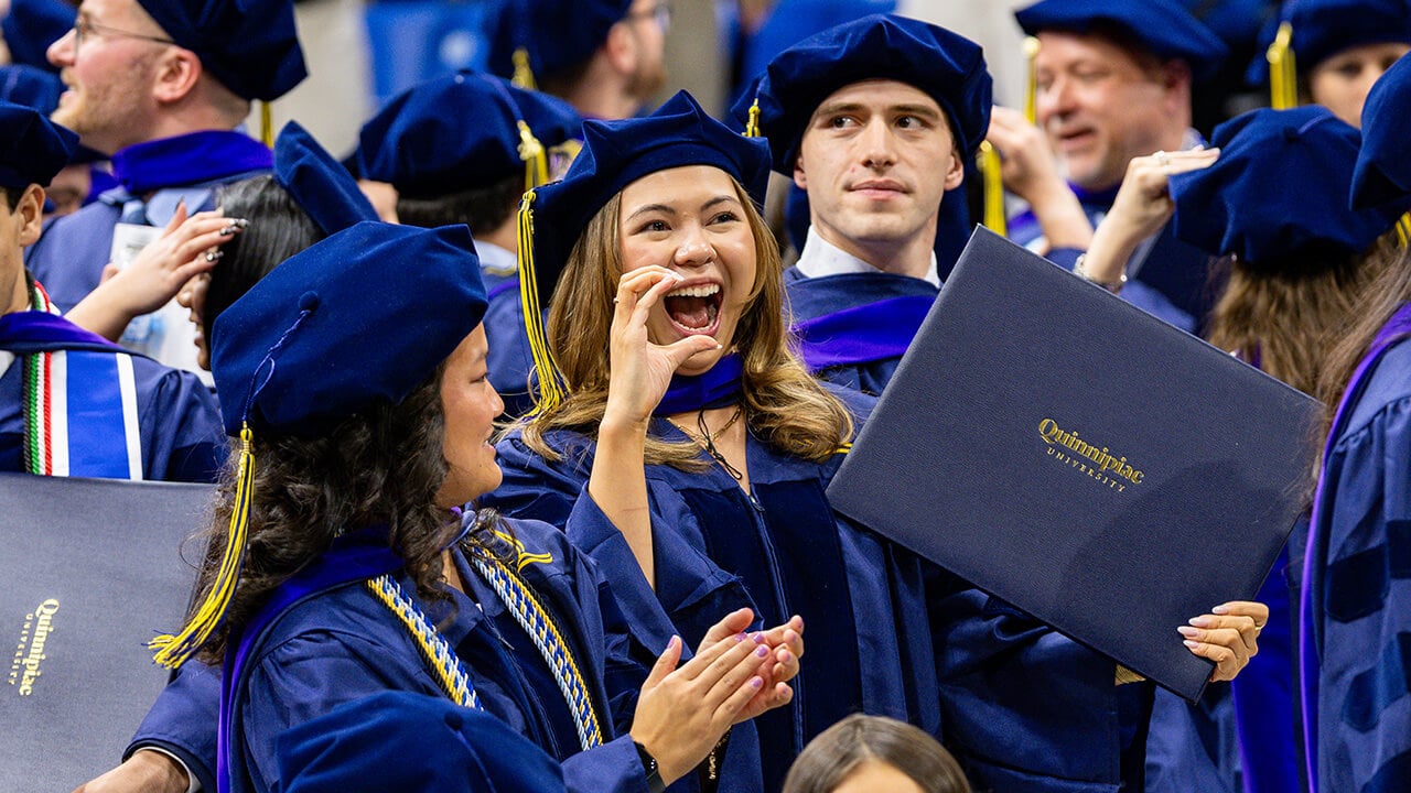 Graduate makes a heart with their hand while holding up diploma