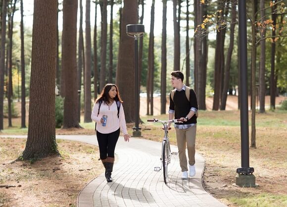 A female and male student talk along a trail. One walks his bike.