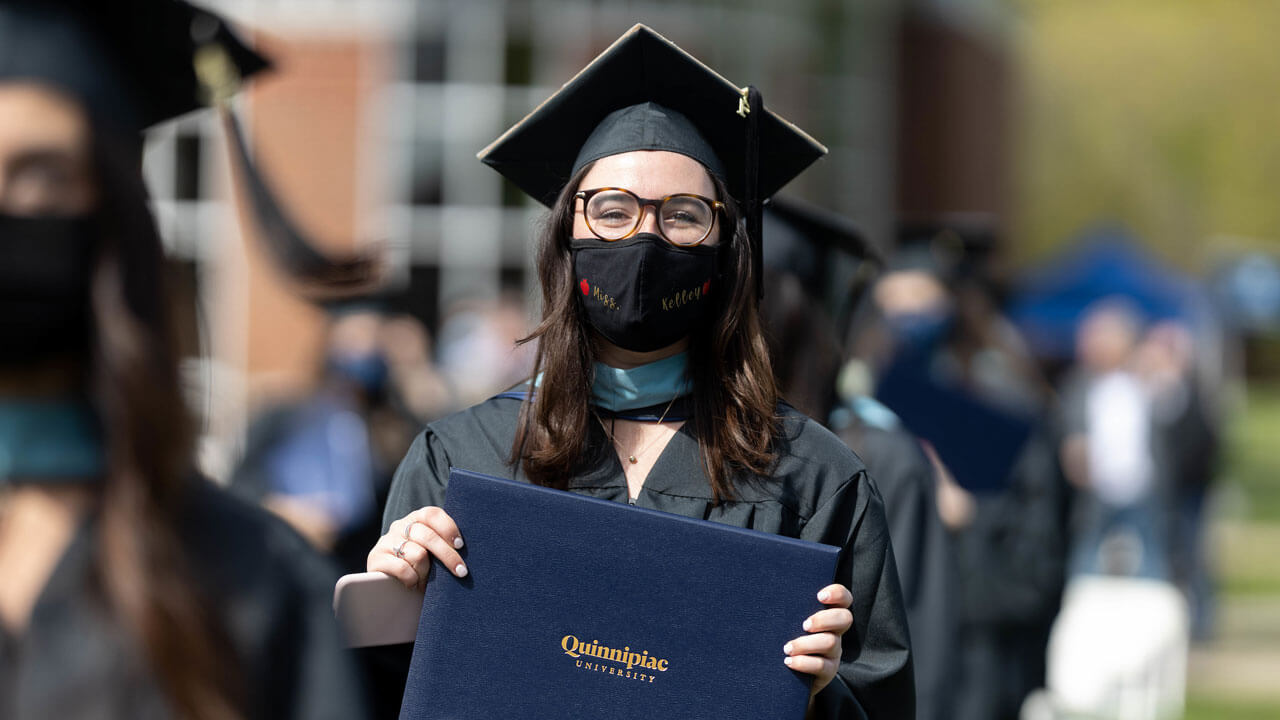 A graduate proudly holds up her diploma cover