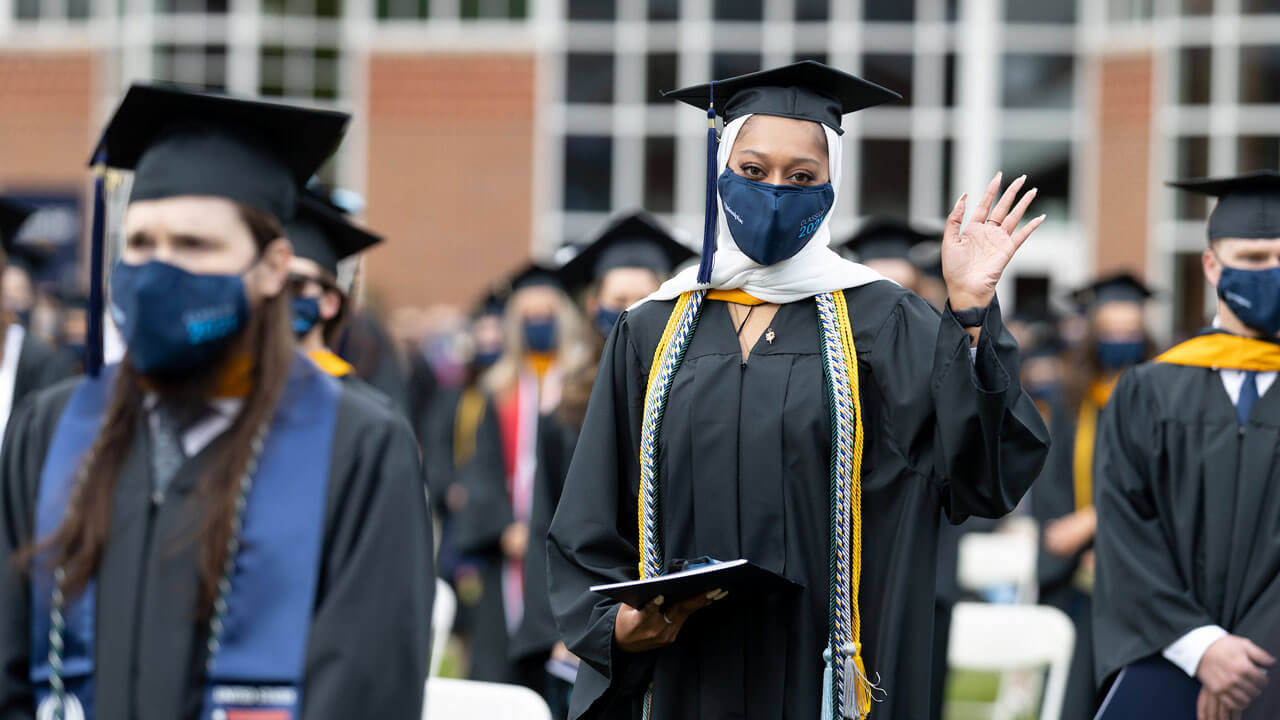 A graduate wearing honors cords waves during Commencement