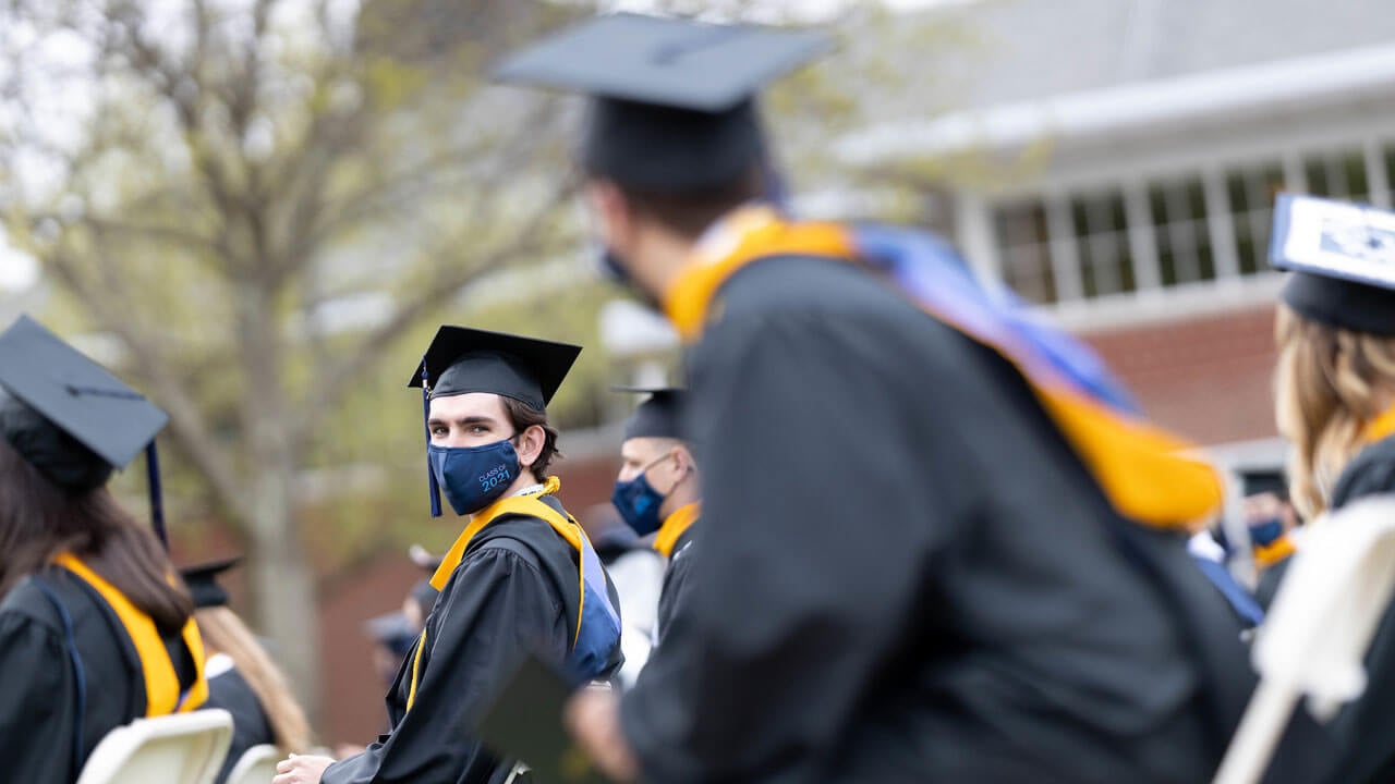 Graduates wearing face coverings sit during the Commencement ceremony
