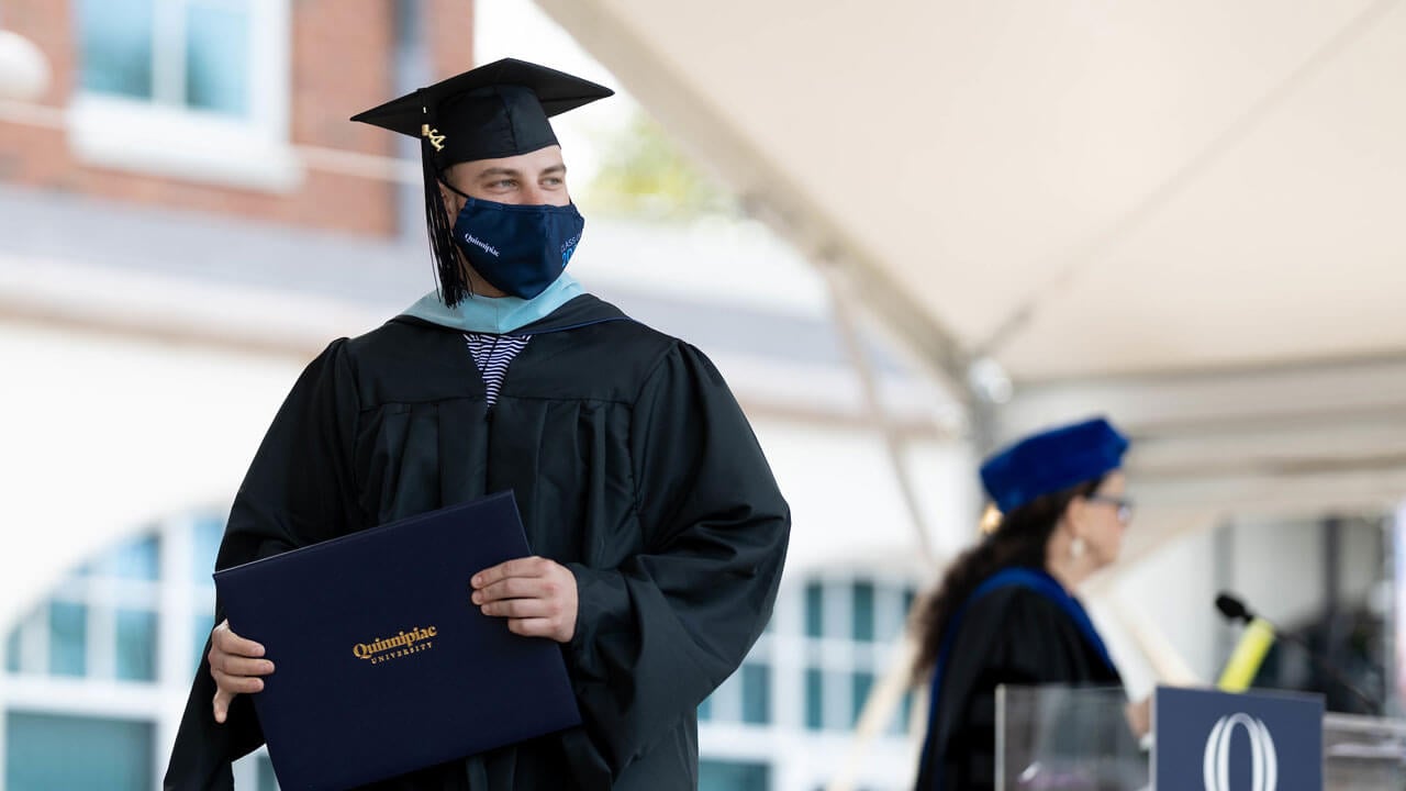 A graduate walks across the stage holding his diploma cover