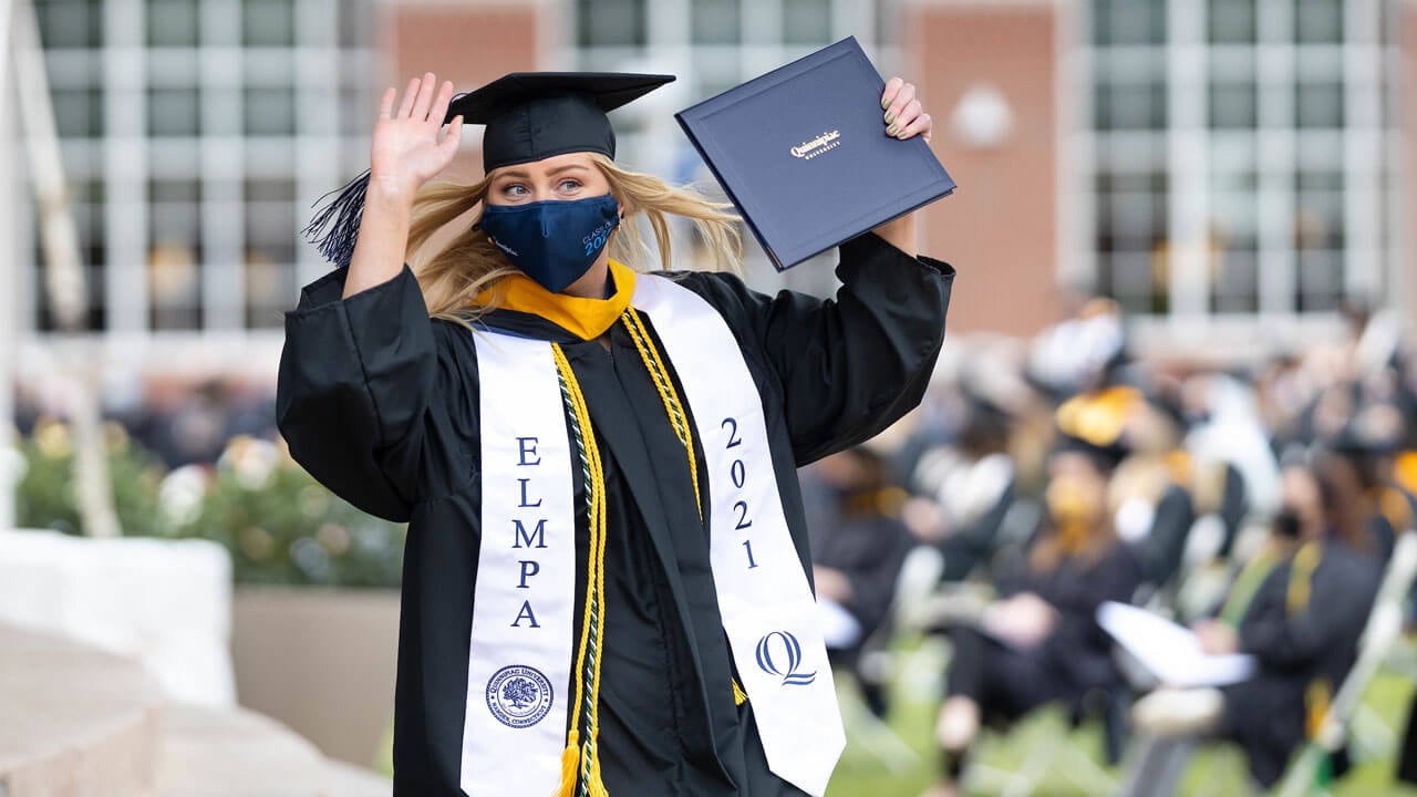 A graduate holds her diploma cover and waves
