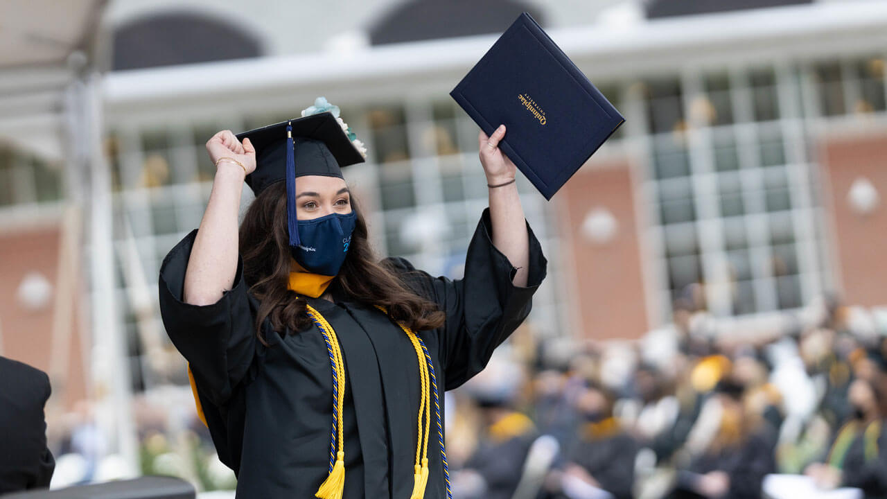 A graduate waves her diploma cover and pumps her arm in celebration