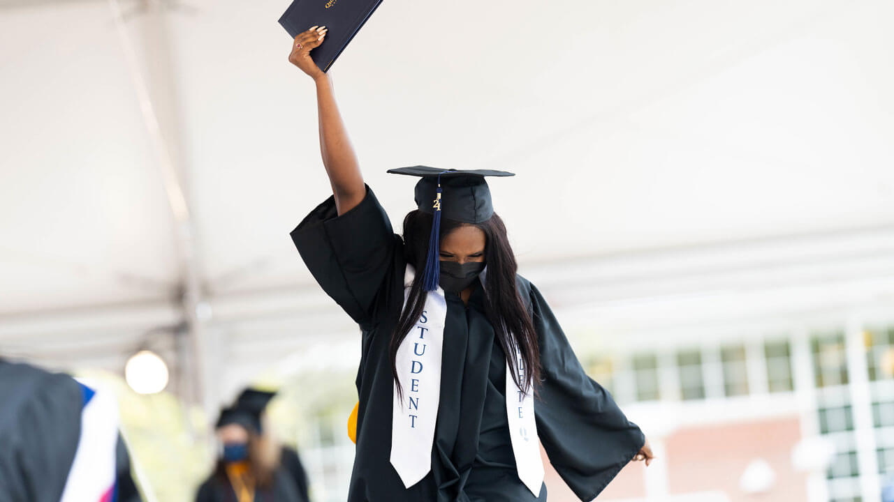 A graduate holds her diploma cover above her head in celebration