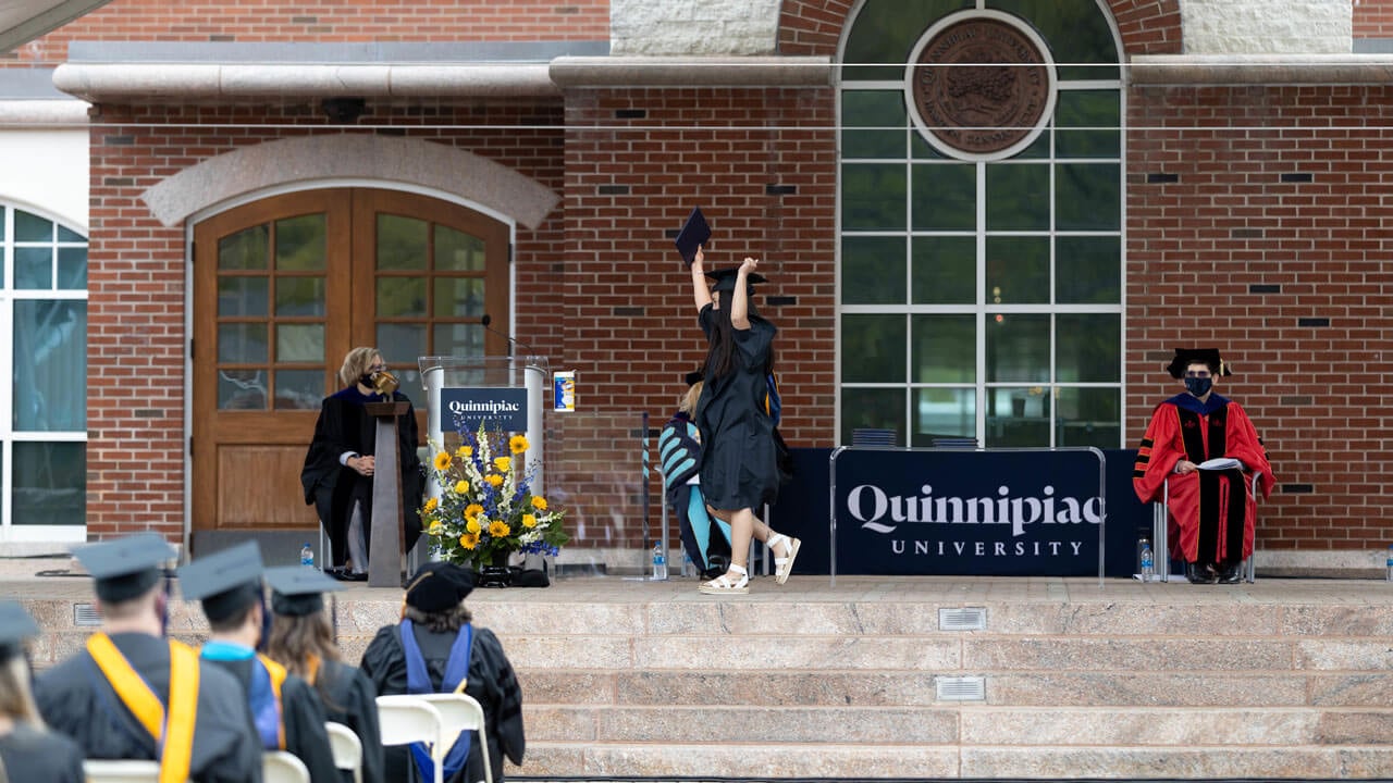 Student throws arms up in air as she walks on podium and receives her degree