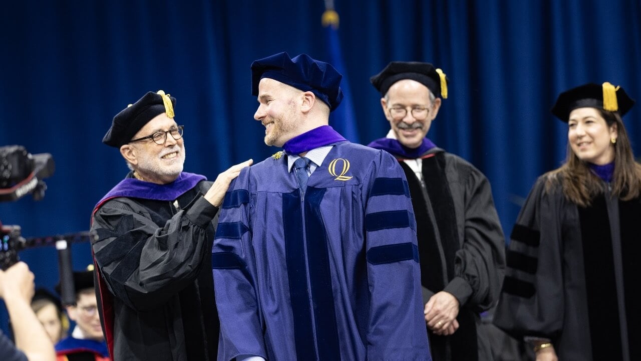 Professor John Thomas and graduate smile at eachother while being hooded