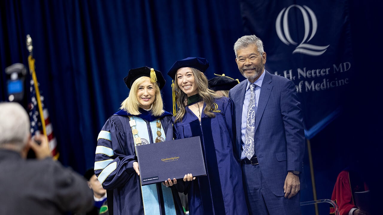 Graduate and guest pose with President Marie Hardin after being hooded