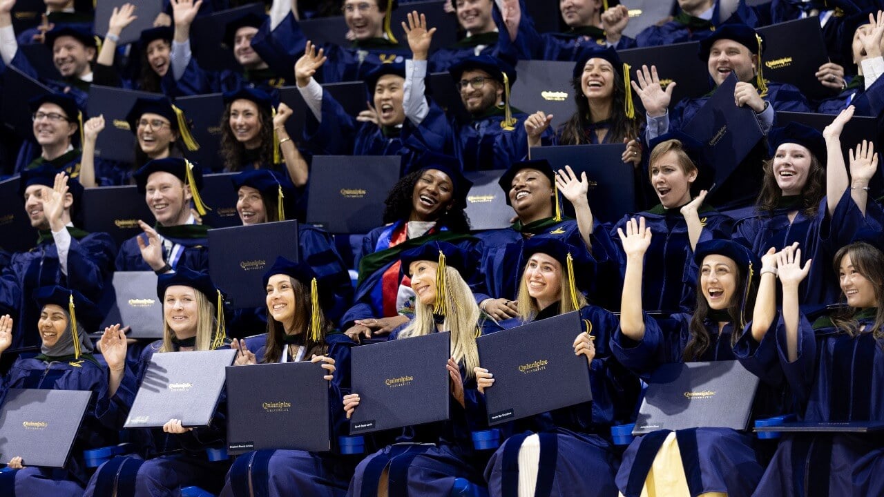Graduates smile and cheer as they hold up their diplomas