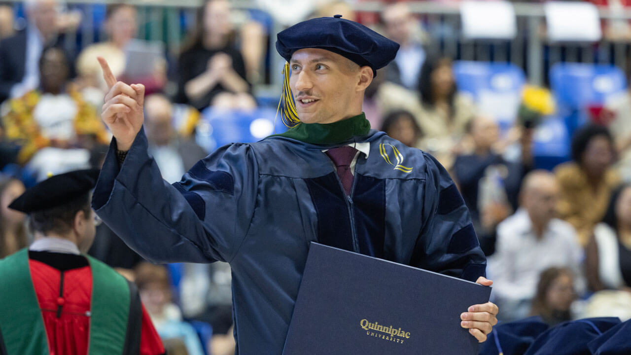 School of Medicine student pointing to the crowd with diploma in hand