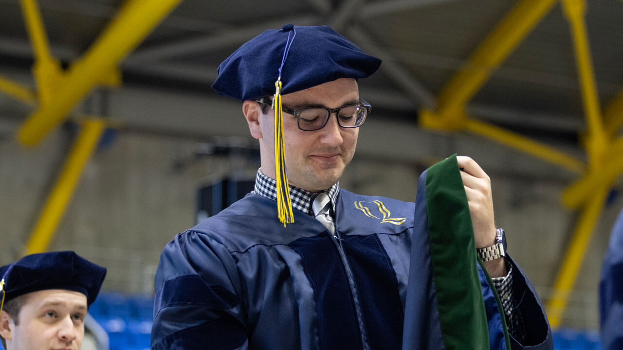 Student looks down smiling in his cap and gown