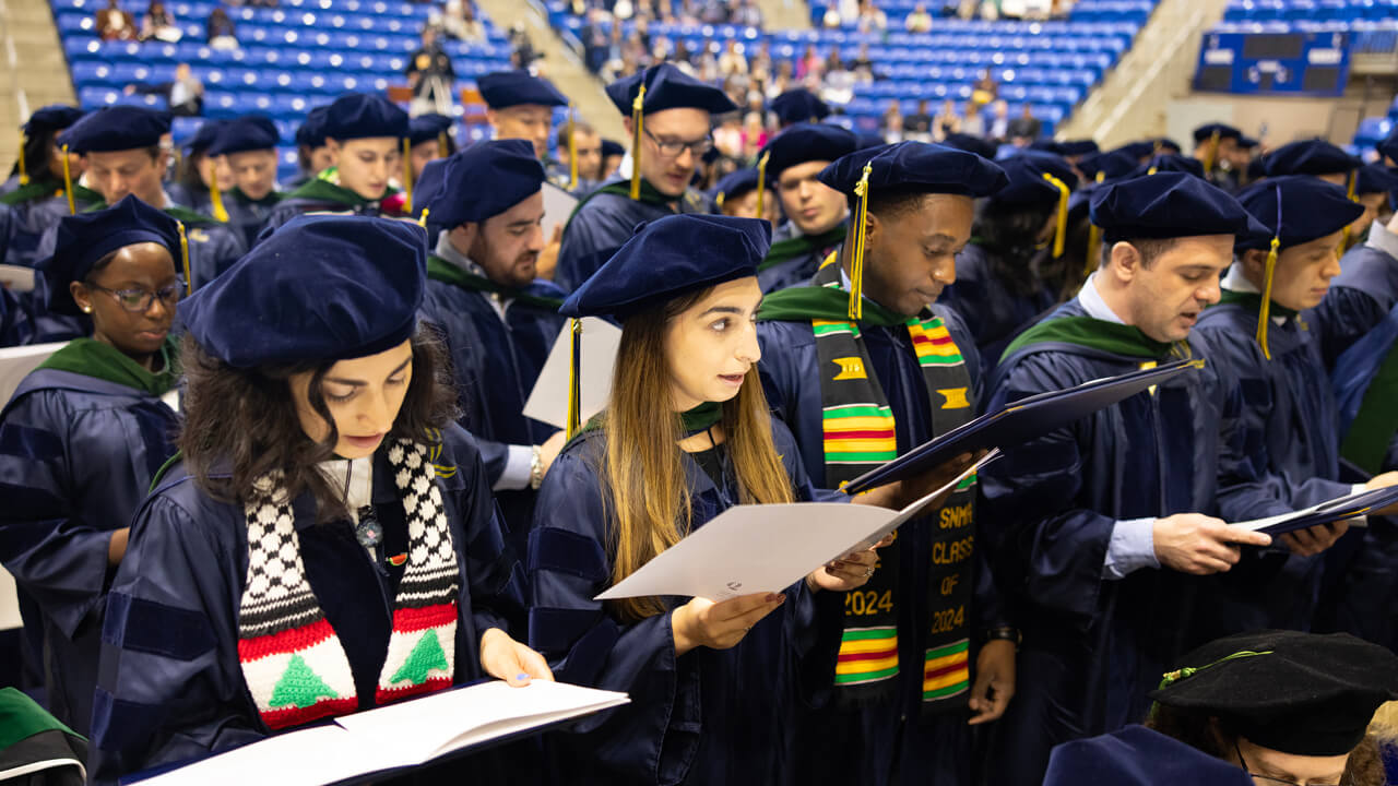 Dozens of graduates read aloud together from papers
