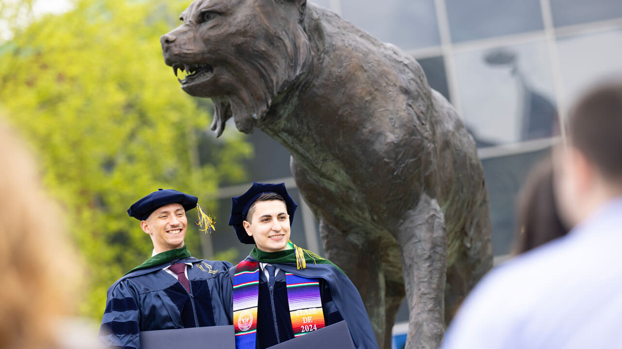 Class of 2024 medical students smiling while holding their diplomas in front of a bobcat statue
