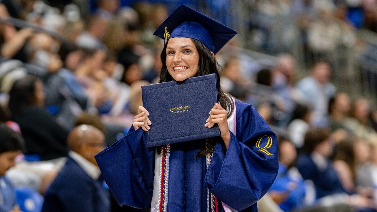 Graduate holds diploma up to face while expressing excitement