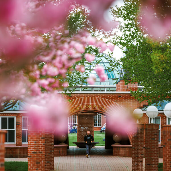 Spring flowers bloom as a student walks outside the School of Business center