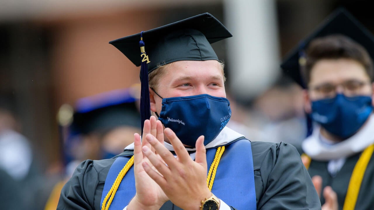 A graduate claps while he sits in his seat during Commecement