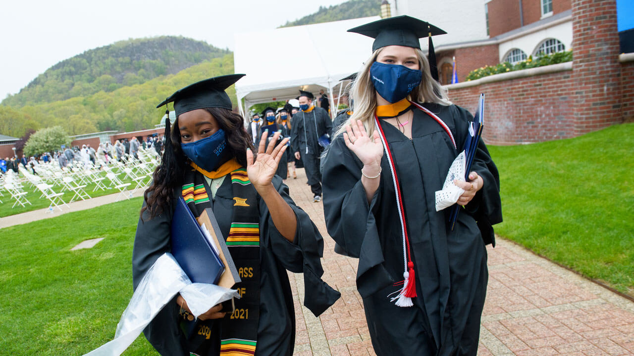 Two graduates wave after receiving their diploma covers