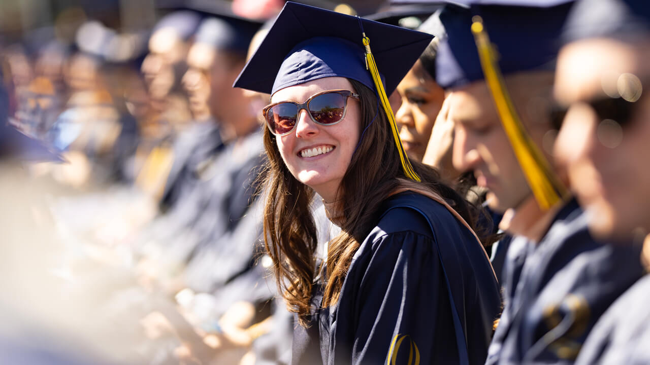 A graduate smiles broadly as she leans forward in her seat