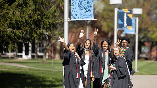 A group of students in caps and gowns waving outside on Quinnipiac's Mount Carmel Campus