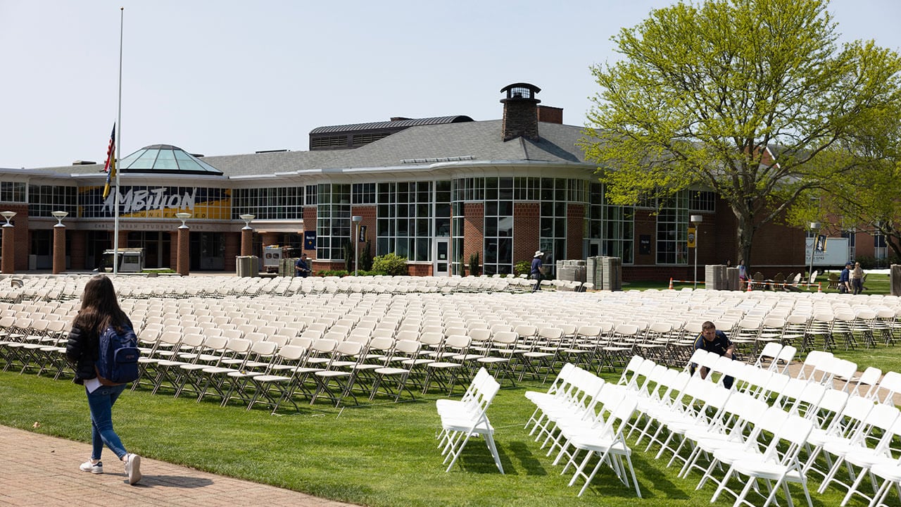 female student walks past rows of white foldable chairs on the quad