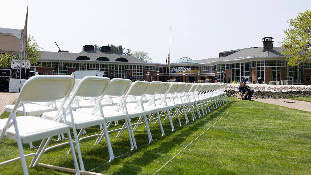 facilities employee lines up a measuring tape near a row of white chairs for commencement