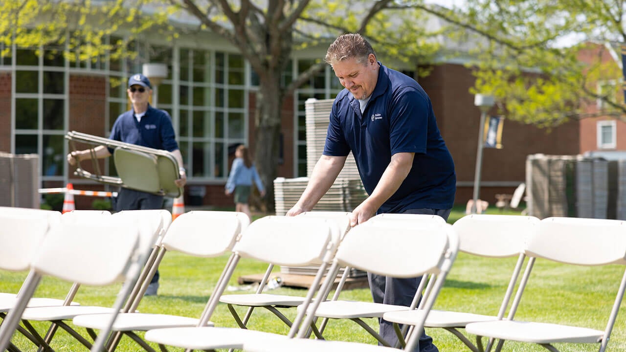 male facilities employee places down a white chair in a row for commencement