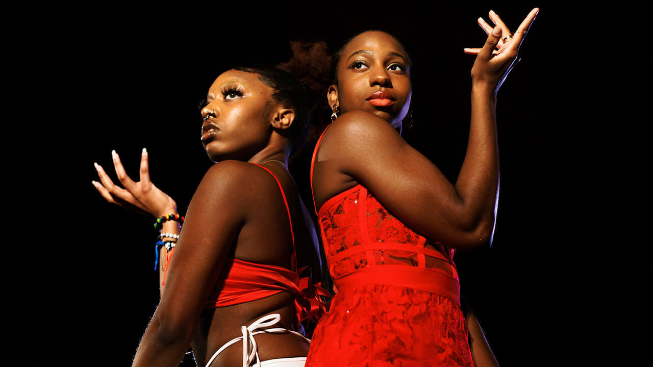 two black woman stand back to back wearing red and posing with one arm raised