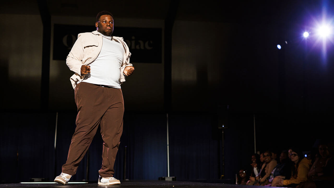 black man wearing a white shirt and jacket with brown pants dances on stage