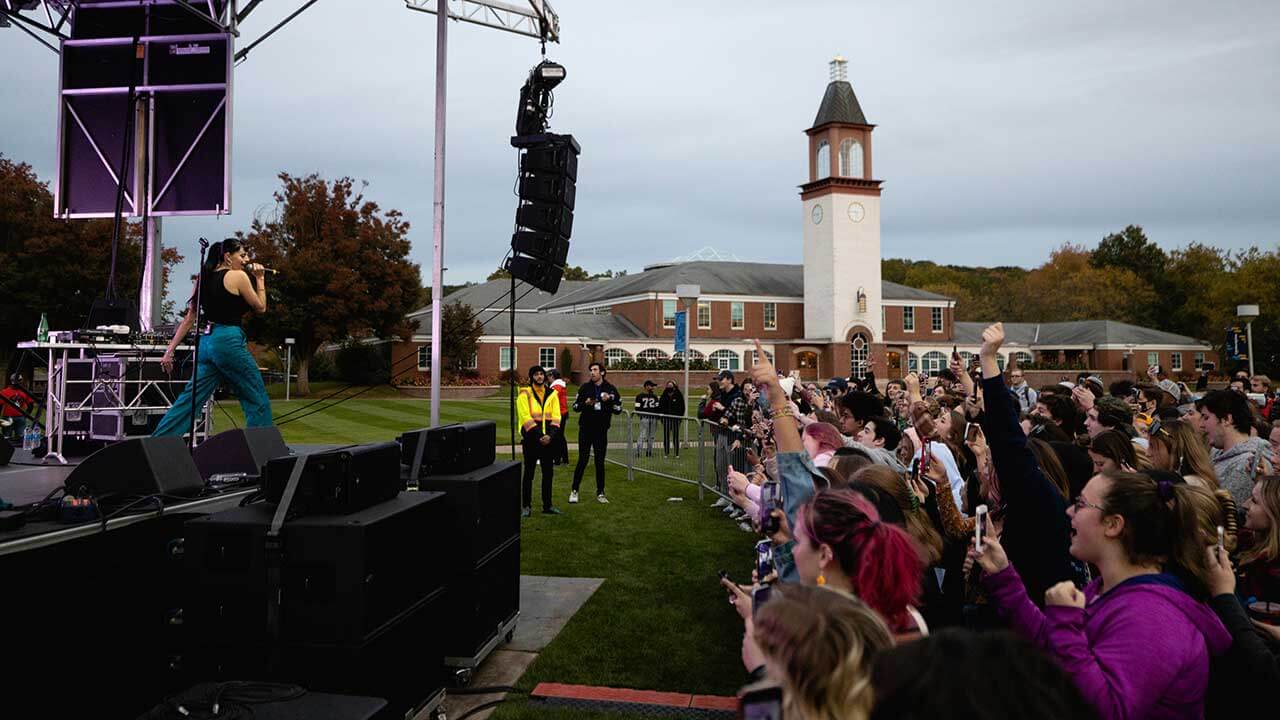 Hundreds of students cheer while a performer sings on an outdoor stage