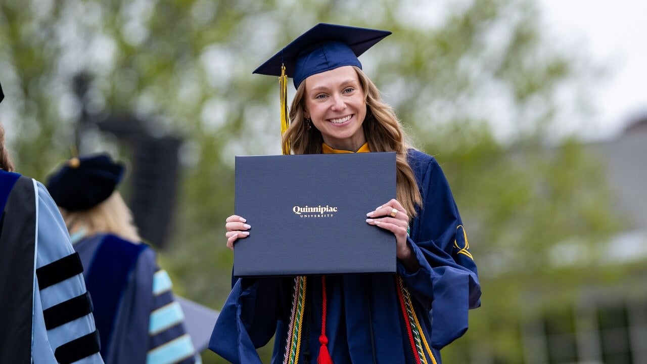 graduate holding diploma and smiling for a photo