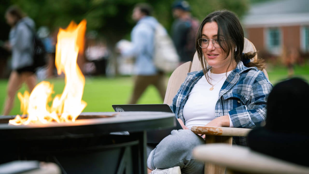 Student sits in front of a fire pit