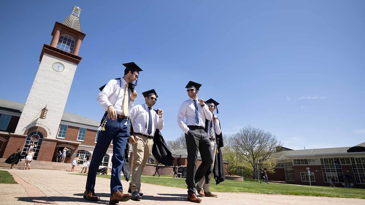 Four students walk across the quad with Commencement robes