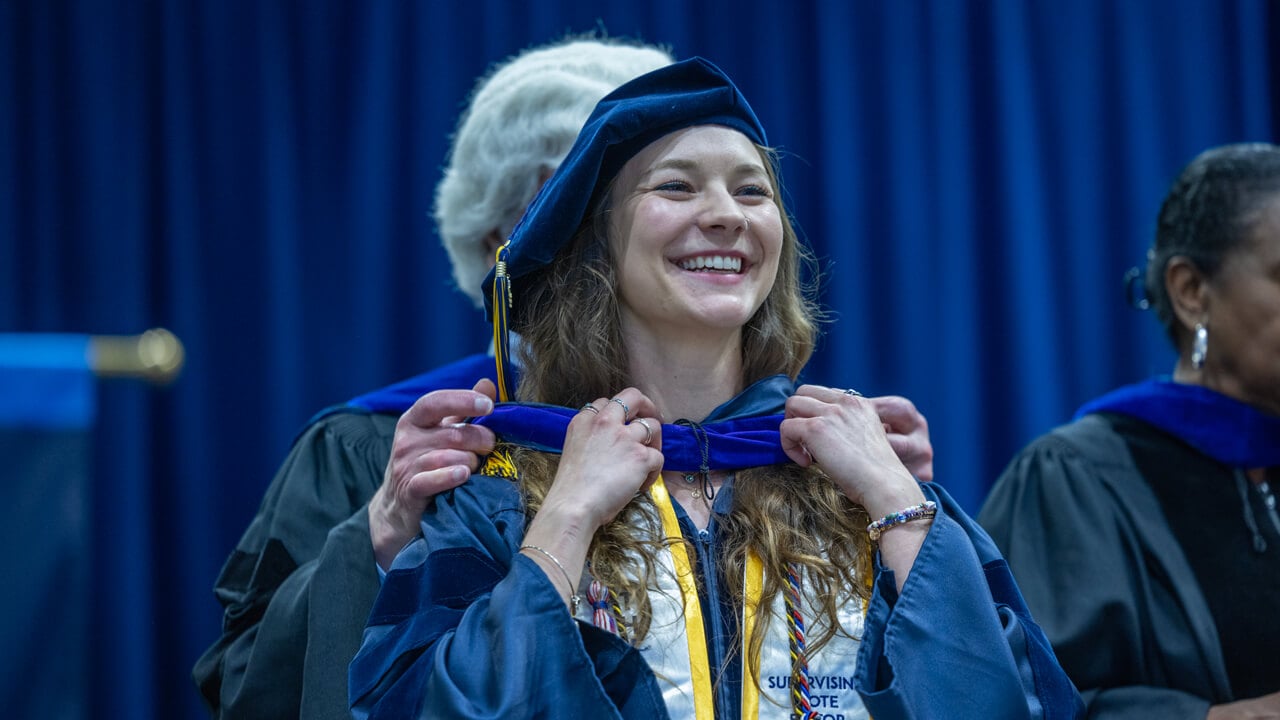 A graduate adjusts her doctoral hood and smiles on stage