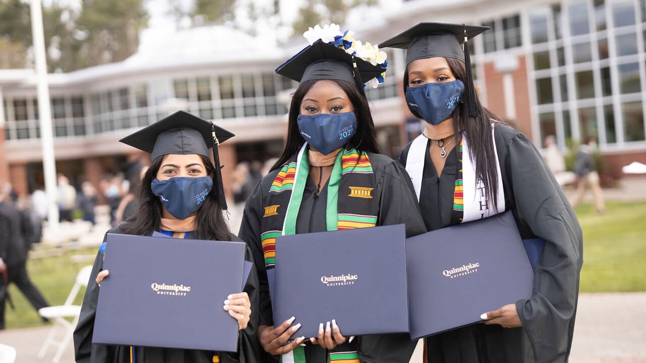 Three grads hold their diploma covers and pose for a photo together
