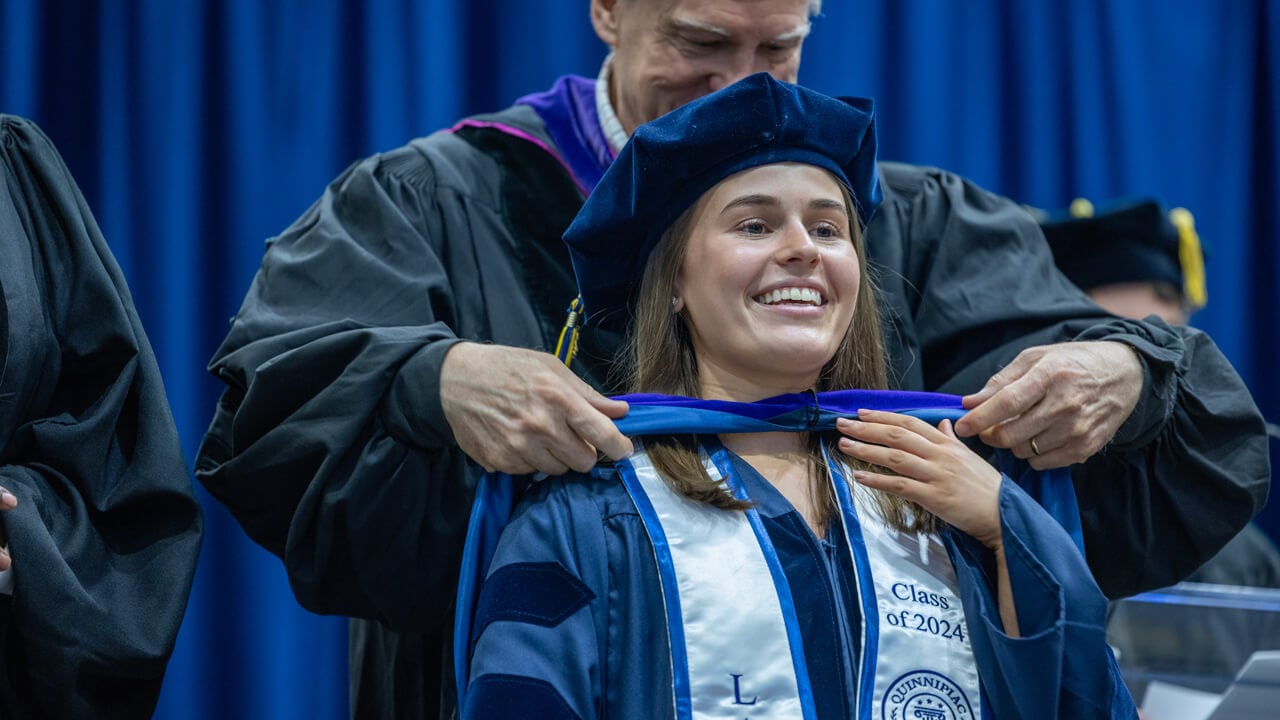 A graduate holds up her hand while a professor places her doctoral hood