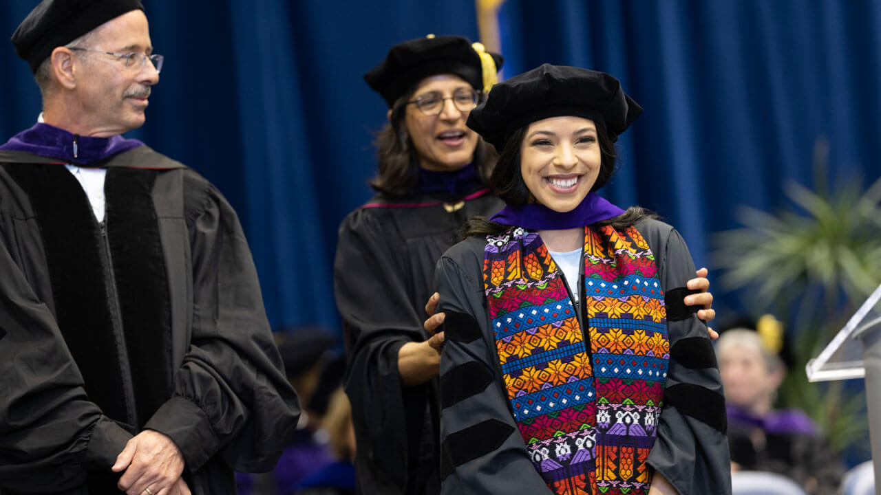 Student receives hood with professors smiling behind her
