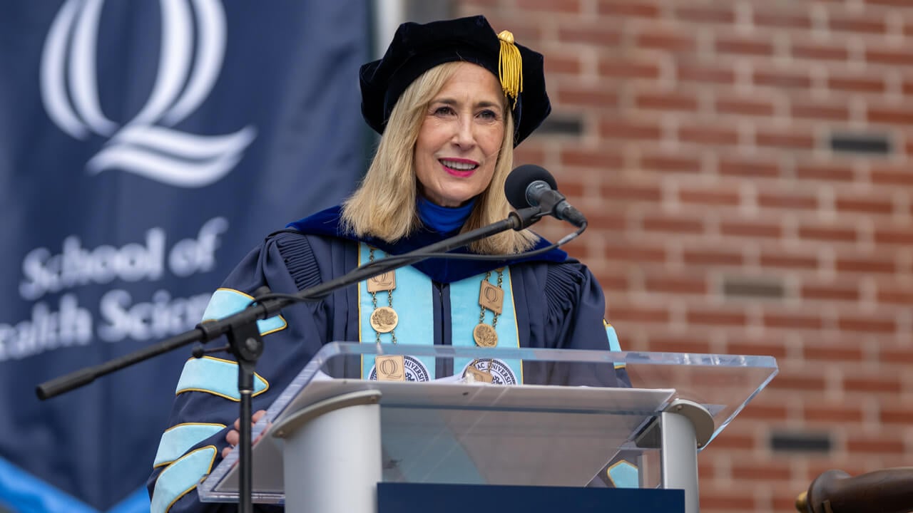 Marie Hardin in her blue Commencement robes speaks at the podium