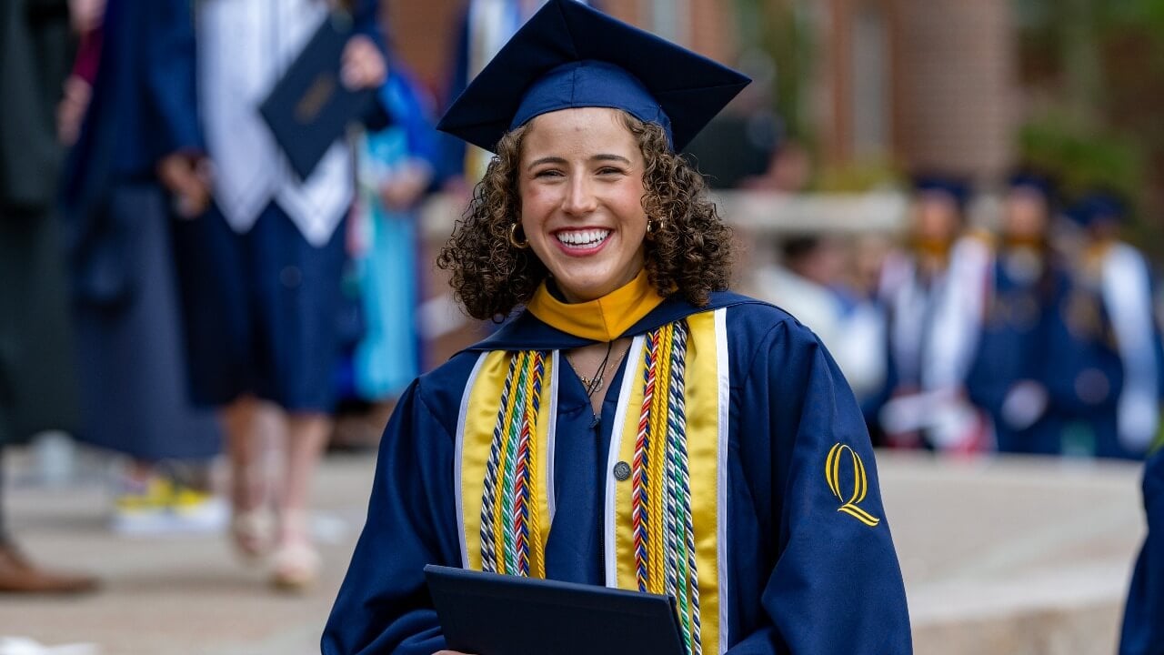 a graduate laughing with joy, holding their diploma smiling to the camera