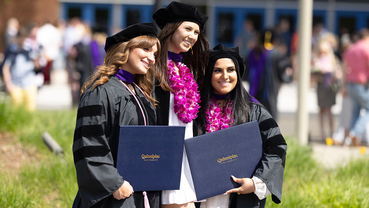 Graduates pose for photos with their diplomas outside