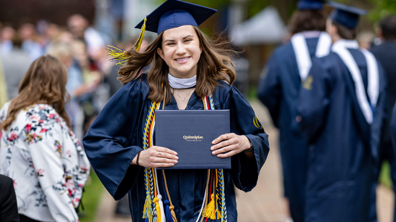 Quinnipiac SOC graduate walking and smiling with her degree up