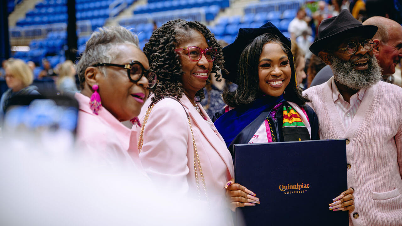 School of Law student smiles with her diploma standing next to her family all dressed in pink