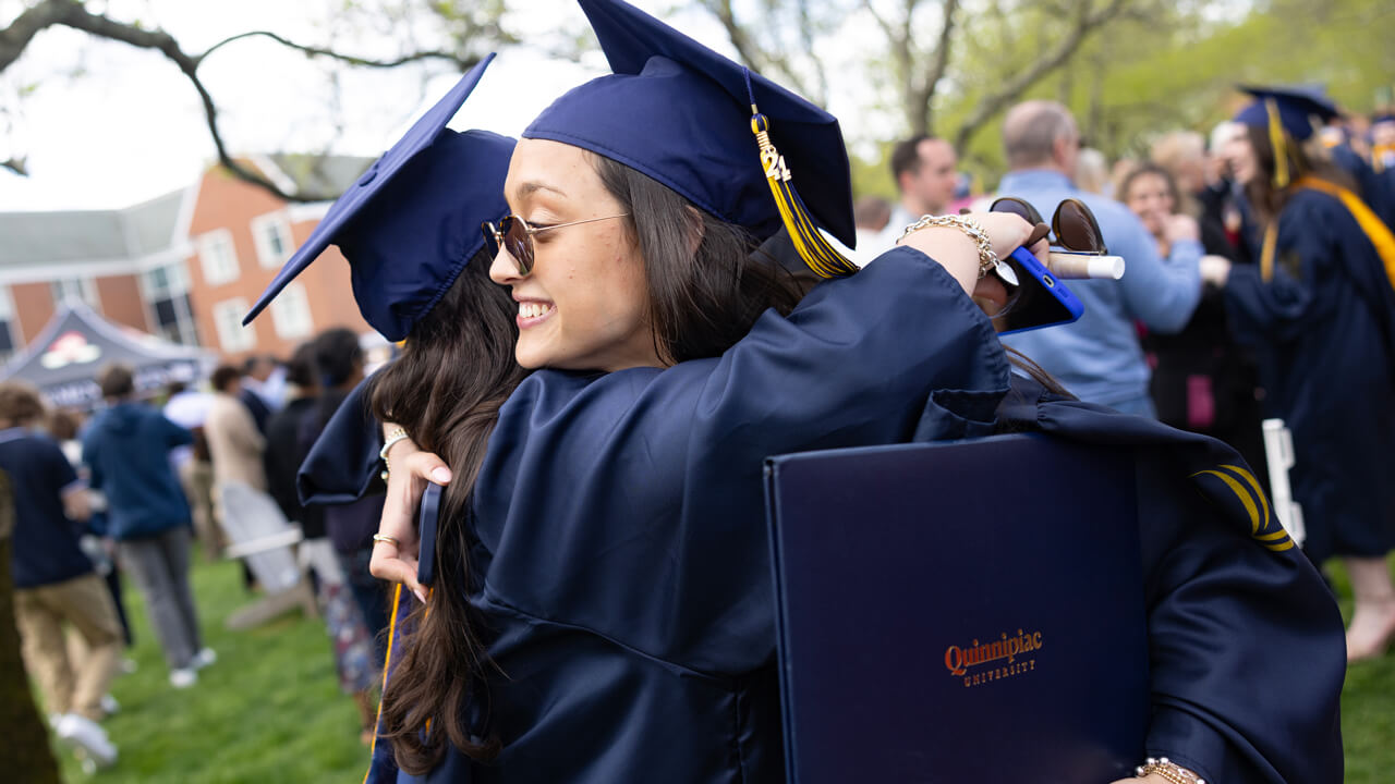 Two graduates hug while they hold their diplomas