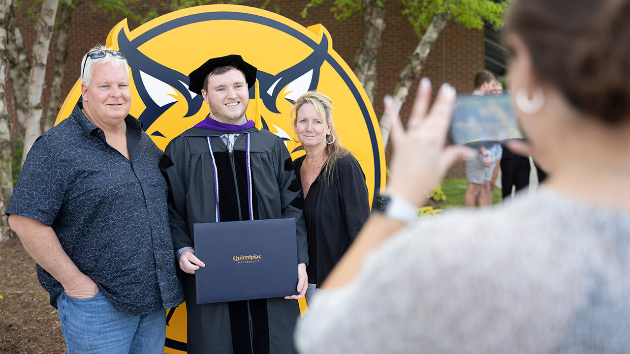 Graduate poses with family in front of bobcat logo photo-op