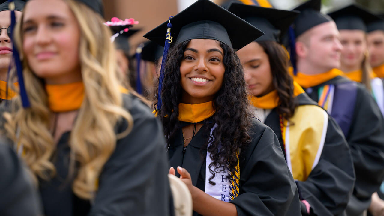 Graduate cheerfully smiling and walking to their seat for commencement